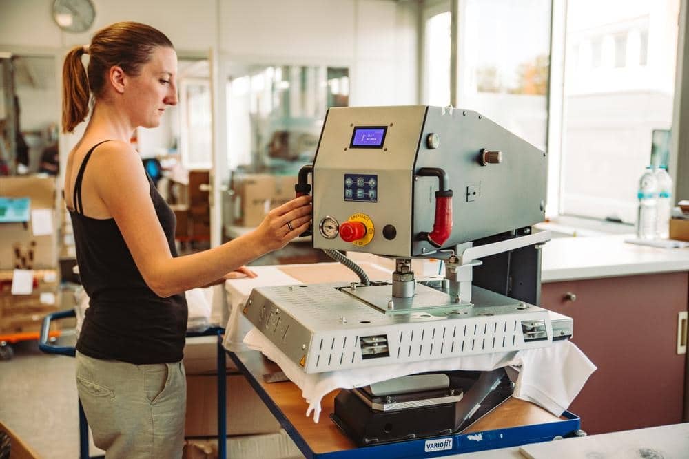 Mitarbeiterin bedient eine Transferpresse zur Veredelung von Textilien.