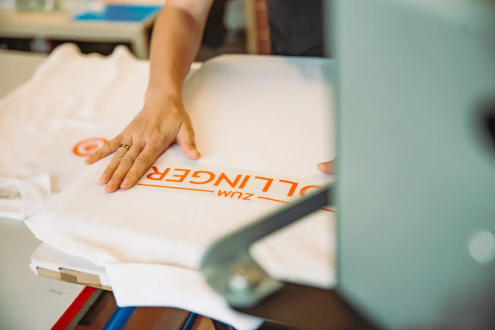 Hand glättet weißes T-Shirt mit orangem Aufdruck auf Transferpresse.