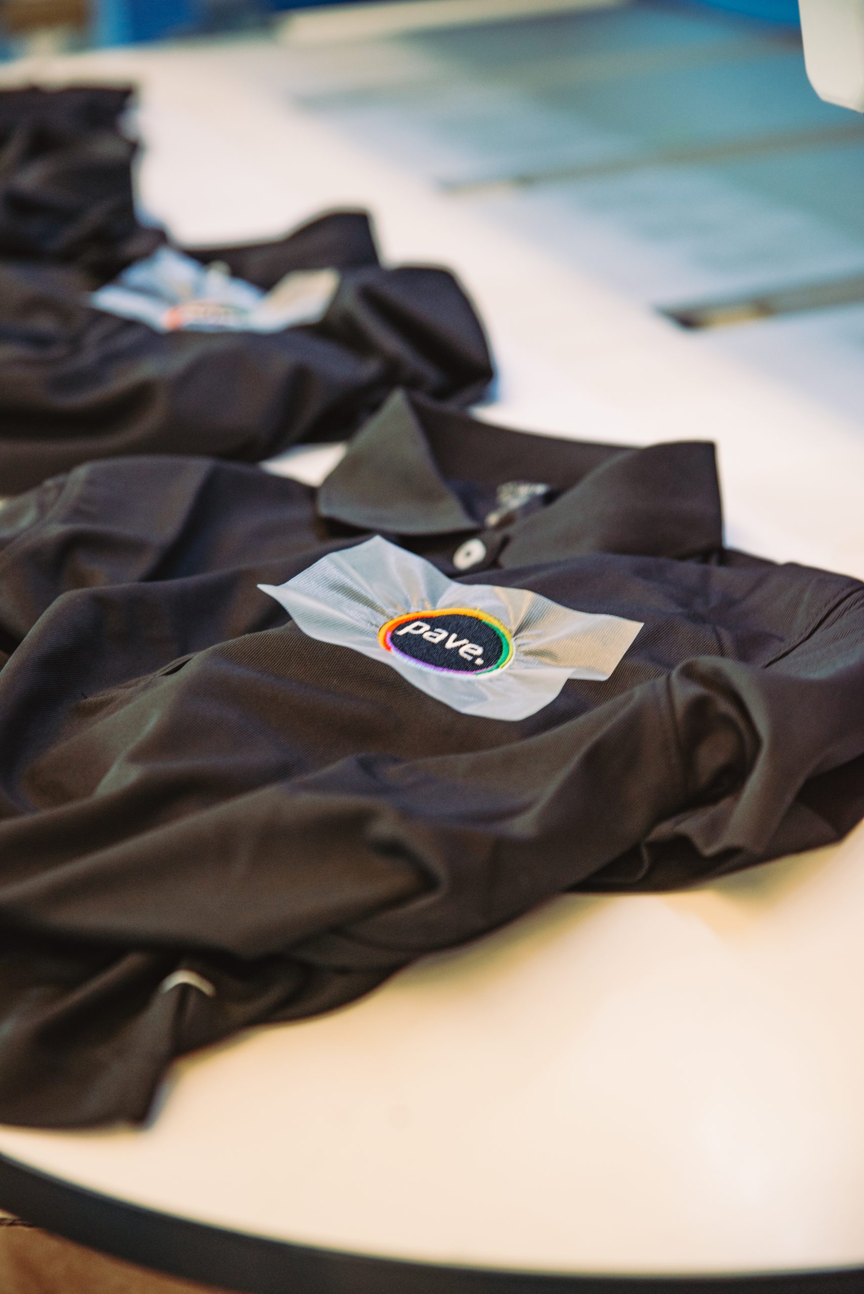 Schwarze Poloshirts mit bunt besticktem Logo auf Werktisch.